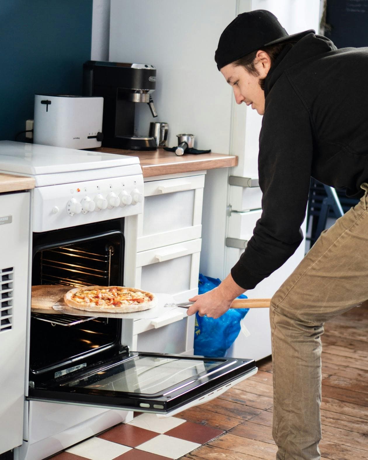 ein junger Mann in einer Küche, der eine Pizza aus dem Ofen holt